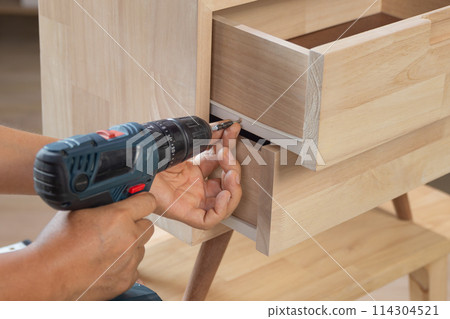Handyman fixing over tight drawer slides rail of bedside table. 114304521
