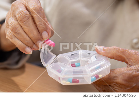 Elderly woman putting pills into pill box for the week. 114304550