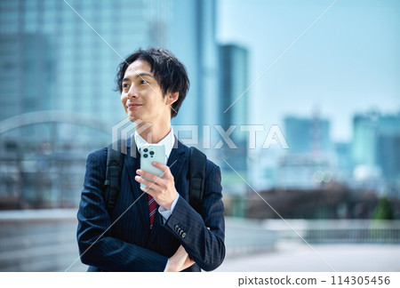 A businessman in a suit carrying a backpack operating a smartphone A businessman in a suit carrying a backpack operating a smartphone 114305456
