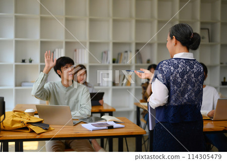 College student man raising his hand to answer question or ask something during class College student man raising his hand to answer question or ask something during class 114305479