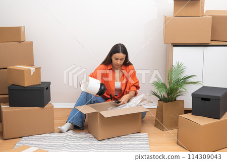 In her new rented home, a young woman's face lights up with delight as she unpacks, savoring the excitement of relocation In her new rented home, a young woman's face lights up with delight as she unpacks, savoring the excitement of relocation 114309043