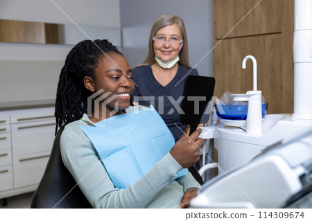 Dark-skinned young woman looking happy after seeing good result of tooth treatment 114309674