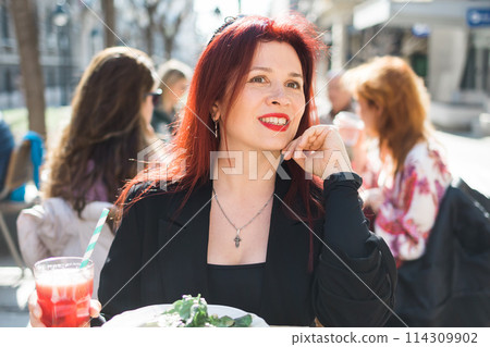 Beautiful happy millennial woman with long red hair enjoying italian pasta in a street cafe Beautiful happy millennial woman with long red hair enjoying italian pasta in a street cafe 114309902