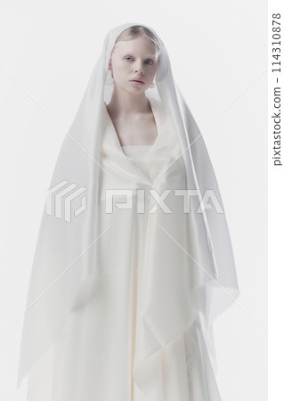 Portrait of young woman with pale skin and blonde hair looking calmly at camera, as maid or angel against white studio background. 114310878