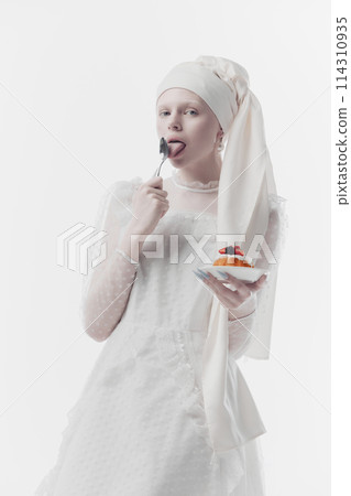 Woman wearing white embroidered dress and a stylish turban, as medieval person eating sweet dessert against white studio background. Woman wearing white embroidered dress and a stylish turban, as medieval person eating sweet dessert against white studio background. 114310935