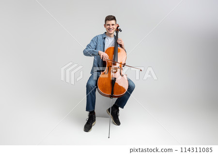 Young man wearing casual clothing playing cello Young man wearing casual clothing playing cello 114311085