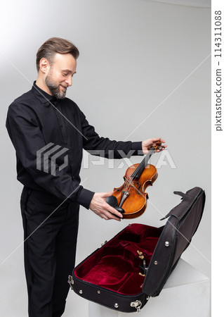 Bearded man artist packing musical instrument in violin case Bearded man artist packing musical instrument in violin case 114311088