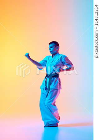 Dynamic martial arts pose, teen boy in motion, training against gradient orange blue background in neon light 114312214