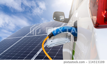 Close up of electric car with a connected charging cable on the background of solar panels.. 114313109