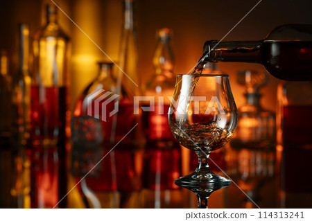 Pouring brandy from a bottle into a glass. 114313241