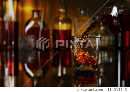 Pouring whiskey from a bottle into a glass. 114313243
