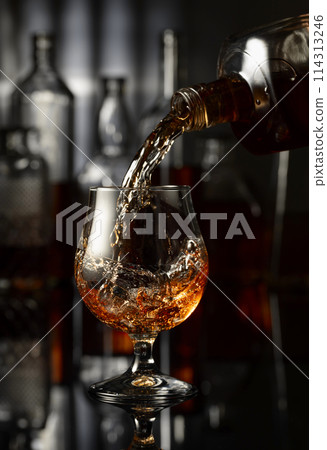 Pouring brandy from a bottle into a glass. Pouring brandy from a bottle into a glass. 114313246