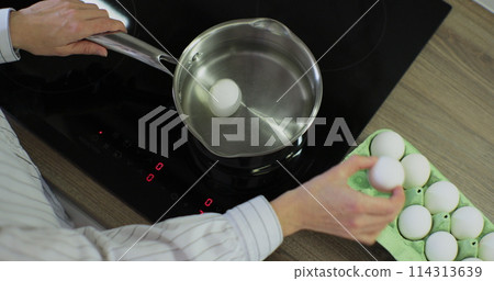 Raw chicken eggs a woman puts in water for cooking. Cooking close-up in the kitchen. Put egg to boil. Raw chicken eggs a woman puts in water for cooking. Cooking close-up in the kitchen. Put egg to boil. 114313639