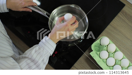 Raw chicken eggs a woman puts in water for cooking. Cooking close-up in the kitchen. Put egg to boil. Raw chicken eggs a woman puts in water for cooking. Cooking close-up in the kitchen. Put egg to boil. 114313645