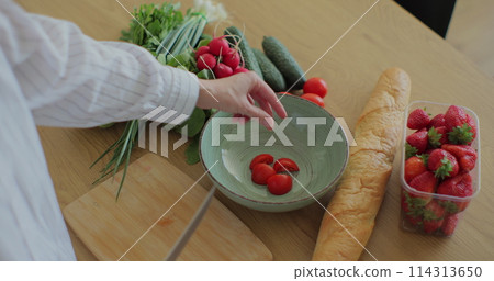 Young woman cutting cherry tomatoes on wood cutting board for fresh salad. Healthy food concept. 114313650