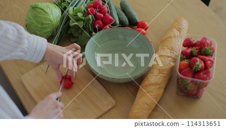 Young woman cutting cherry tomatoes on wood cutting board for fresh salad. Healthy food concept. Young woman cutting cherry tomatoes on wood cutting board for fresh salad. Healthy food concept. 114313651