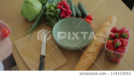 Young woman cutting cherry tomatoes on wood cutting board for fresh salad. Healthy food concept. 114313652