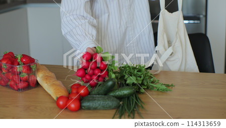 Young woman is unpacking products and vegetables in the modern kitchen on wooden table. Online shopping, food delivery. Young woman is unpacking products and vegetables in the modern kitchen on wooden table. Online shopping, food delivery. 114313659