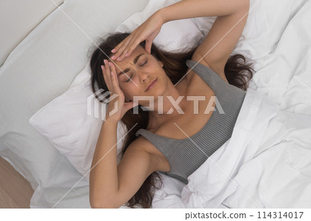 Depressed young woman lies on bed closing eyes and pressing fingers to temples attractive female suffers from headache and insomnia symptom of disease Depressed young woman lies on bed closing eyes and pressing fingers to temples attractive female suffers from headache and insomnia symptom of disease 114314017