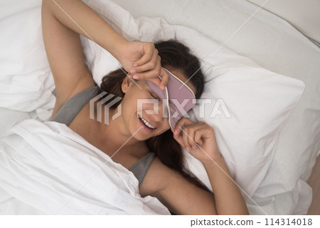 Beaming with happiness, she unveils her eyes from the sleep mask, feeling revitalized by the morning's energy.top view Beaming with happiness, she unveils her eyes from the sleep mask, feeling revitalized by the morning's energy.top view 114314018