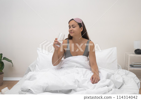 With a smile, she presents a glass of pure water in bed, rejuvenating herself after a restful night's sleep.  114314042