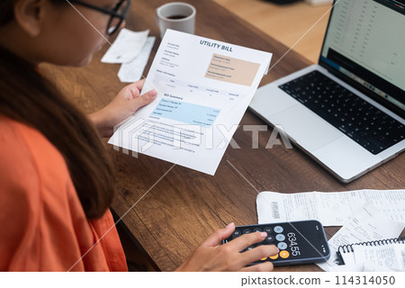 woman, home-bound, settles household utility bills online via her laptop, clutching payment receipts, ensuring timely payments 114314050