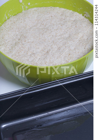 Baking bread at home. Wholemeal dough lies in a container. Near metal baking dish for bread. 114314244