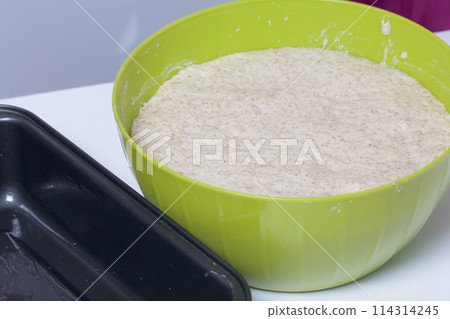 Baking bread at home. Wholemeal dough lies in a container. Near metal baking dish for bread. Baking bread at home. Wholemeal dough lies in a container. Near metal baking dish for bread. 114314245