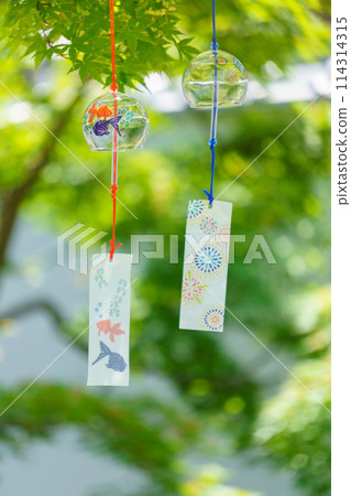 Glass wind chimes swaying under green maples Glass wind chimes swaying under green maples 114314315