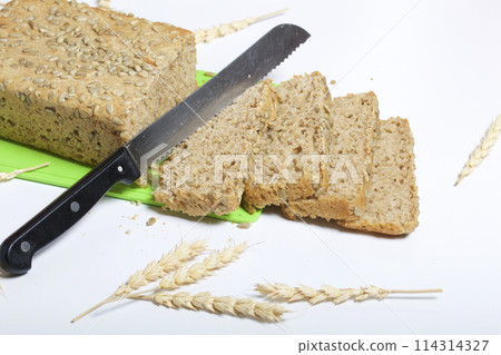 Baking bread at home. A loaf of freshly baked wholegrain bread with sunflower seeds lies on a cutting board. Bread slices and a knife are visible. Baking bread at home. A loaf of freshly baked wholegrain bread with sunflower seeds lies on a cutting board. Bread slices and a knife are visible. 114314327