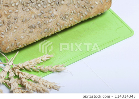 Baking bread at home. A loaf of freshly baked wholegrain bread with sunflower seeds lies on a cutting board. Nearby lies a spikelets. Baking bread at home. A loaf of freshly baked wholegrain bread with sunflower seeds lies on a cutting board. Nearby lies a spikelets. 114314343