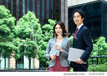 Male and female business people standing with computers in an office building 114315050