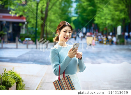 購物時操作智慧型手機的時尚年輕女性 購物時操作智慧型手機的時尚年輕女性 114315659