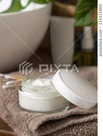 Cosmetic cream jar on beige towels near basin and green monstera in bath, lid mockup 114315869