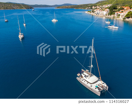 Scenic aerial view many yachts boats moored at Croatian bay harbor shore blue turquoise clear water at bright summer sunny day. Top above Mediterranean sea marina. Boat vessel charter service Scenic aerial view many yachts boats moored at Croatian bay harbor shore blue turquoise clear water at bright summer sunny day. Top above Mediterranean sea marina. Boat vessel charter service 114316027