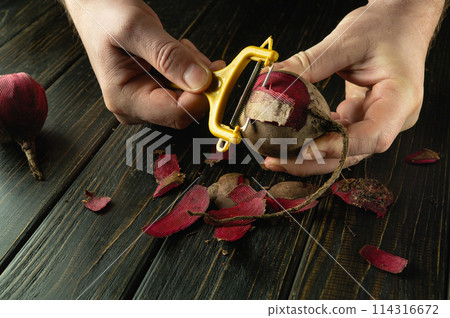 Close-up of a cook hands using a peeler to peel raw beet to prepare lunch. Vegetable menu concept for restaurant or hotel on black background Close-up of a cook hands using a peeler to peel raw beet to prepare lunch. Vegetable menu concept for restaurant or hotel on black background 114316672