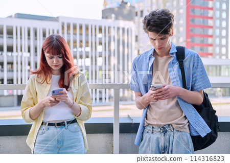 Teenage friends guy and girl using smartphones, urban outdoor Teenage friends guy and girl using smartphones, urban outdoor 114316823