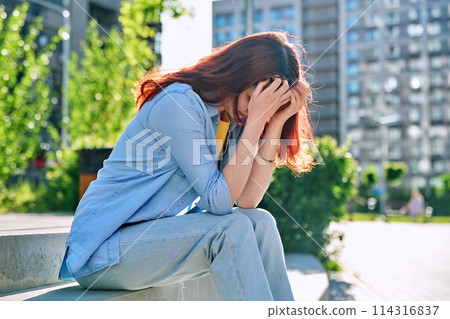 Upset sad unhappy young female sitting outdoor on steps 114316837