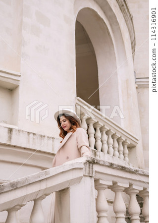 woman in elegant coat and hat against an intricate architectural backdrop, harmoniously blending modern fashion with historical allure. The soft daylight adds to its timeless appeal. woman in elegant coat and hat against an intricate architectural backdrop, harmoniously blending modern fashion with historical allure. The soft daylight adds to its timeless appeal. 114316901