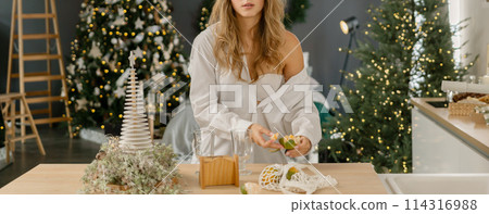 Woman Kitchen Christmas decor in white shirt, peeling tangerines. Illustrating New Year's mood holiday preparations Woman Kitchen Christmas decor in white shirt, peeling tangerines. Illustrating New Year's mood holiday preparations 114316988