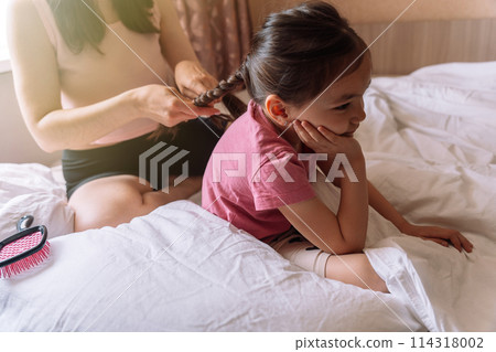 Mom braids her daughter's hair while sitting in bed Mom braids her daughter's hair while sitting in bed 114318002