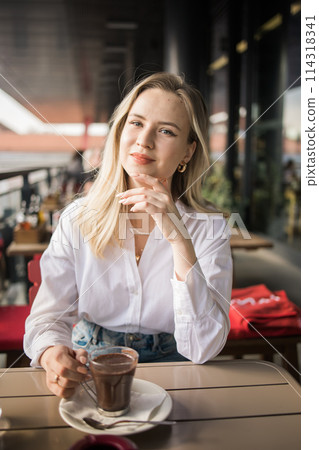 Gen z blonde woman drinks hot chocolate in summer cafe. Tasty beverage and break concept. Generation z people Gen z blonde woman drinks hot chocolate in summer cafe. Tasty beverage and break concept. Generation z people 114318341