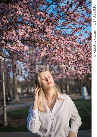 Woman with cherry flowers surrounded by blossoming trees copy space. Beauty and seasonal change and spring bloom season concept. 114318930