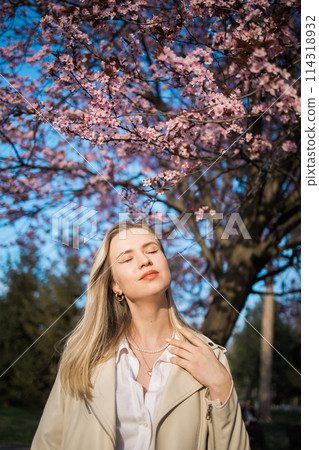 Fashion outdoor photo of beautiful woman with blond hair in elegant suit posing in spring flowering park with blooming cherry tree. Copy space and empty place for advertising text 114318932