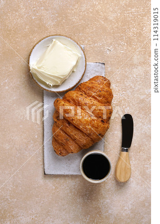 freshly baked croissants and coffee cup and butter on cutting board on brown table , top view freshly baked croissants and coffee cup and butter on cutting board on brown table , top view 114319015
