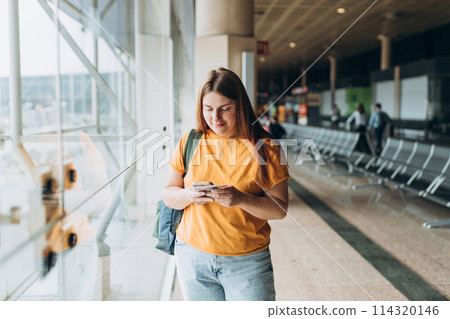 Happy Caucasian Woman waiting at Flight Gates for Plane Boarding, Uses Mobile Smartphone. 30s female Checking Trip Destination on Internet, concept of traveling 114320146