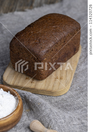 a square dark loaf of bread on the table 114320726