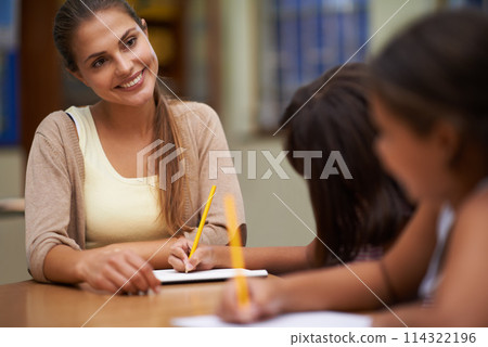Happy teacher, students and writing in class for education, learning or tutoring at school. Woman, mentor or educator smile for helping kids or children with books in study, library or classroom 114322196