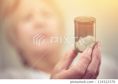 Medicine to manage her chronic health condition. an elderly woman holding a container of medicine. 114322570