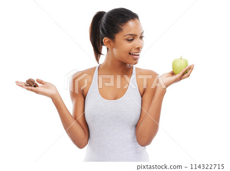 Man, apple and chocolate for healthy food choice or thinking of diet on a white background. African person with sweets versus green fruit in palm for detox decision or lose weight challenge in studio 114322715